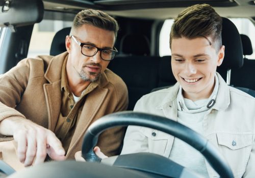 handsome father pointing on something while teaching smiling teen son driving car